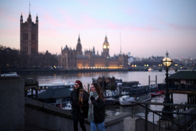 People walk along the South Bank with the Houses of Parliament in the distance in London
