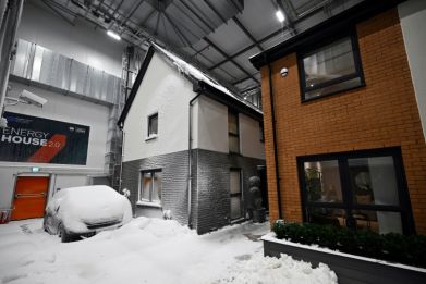 Simulated snow covers a car and the walls of one of two houses built in a lab to develop future heating solutions that will use less energy and help meet climate goals