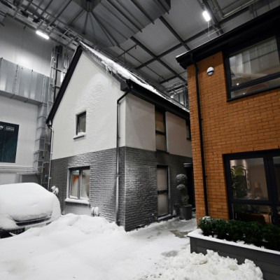 Simulated snow covers a car and the walls of one of two houses built in a lab to develop future heating solutions that will use less energy and help meet climate goals