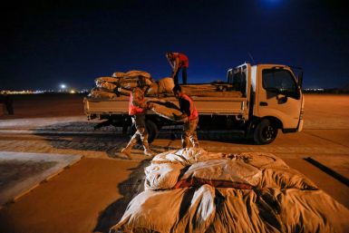 Iraqi soldiers and Iraqi Red Crescent society workers unload trucks with aid that will be shipped on a plane of emergency relief to Syria, in Baghdad