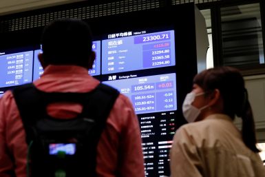 TV crews talk in front of  a large screen showing stock prices at the Tokyo Stock Exchange in Tokyo