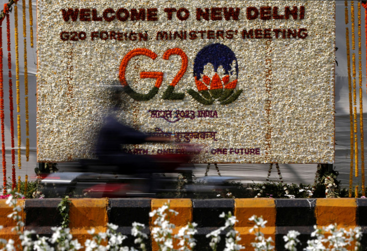 A motorist rides past a hoarding decorated with flowers to welcome G20 foreign ministers in New Delhi