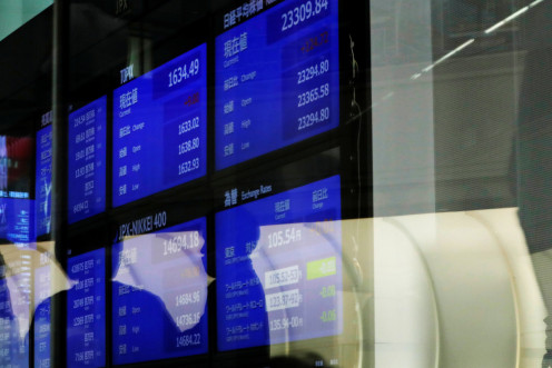 People are reflected on a glass in front of a large screen showing stock prices at the Tokyo Stock Exchange after market opens in Tokyo