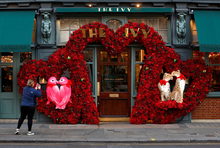 A woman photographs a Valentines Day floral display attached to the facade of a restaurant in London