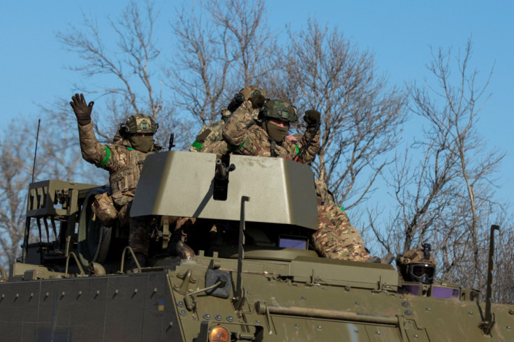 Ukrainian service members gesture as they ride atop of a M113 armoured personnel carrier outside of the frontline town of Bakhmut