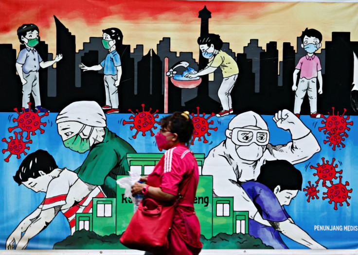 A woman wearing a protective face mask walks past a mural promoting awareness of the coronavirus disease (COVID-19) outbreak, in Jakarta