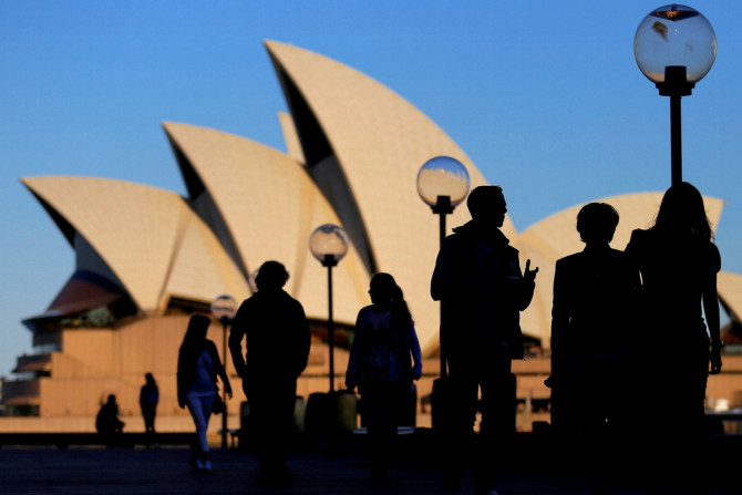 People are silhouetted against the Sydney Opera House at sunset in Australia