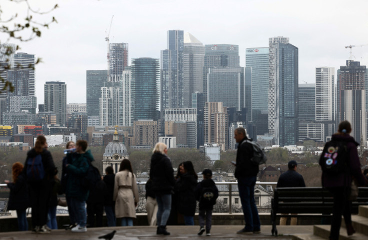 People lookout from Greenwich Park, with the Canary Wharf financial district in the distance, in London
