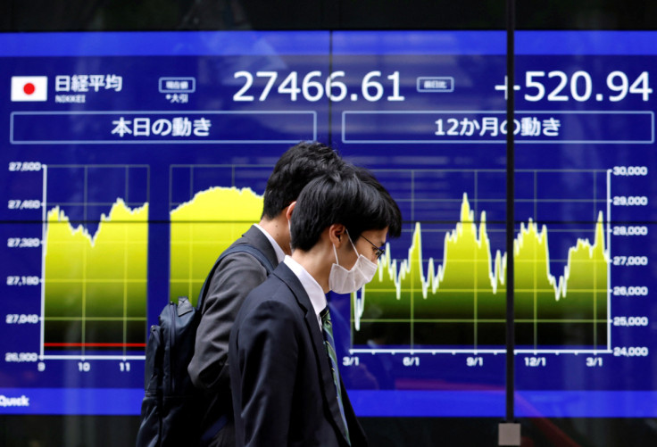 Passersby walk past an electric monitor displaying Japan's Nikkei share average and recent movements outside a bank in Tokyo