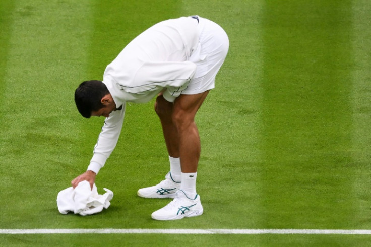 Wipe out: Novak Djokovic attempts to dry the grass of Center Court with a towel