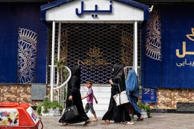 Afghan women walk past a closed beauty parlour in Kabul on July 25, 2023