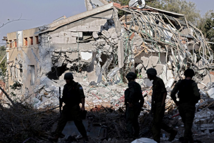 Israeli soldiers walk past a destroyed house in kibbutz Beeri