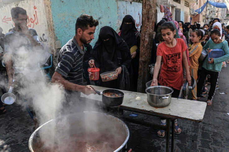 Palestinians queue to receive a portion of food at a makeshift charity kitchen in Rafah