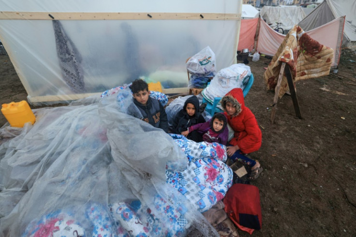 Young Palestinians sit outside on mattresses covered with plastic at a camp for displaced people in Rafah, in the southern Gaza Strip where most civilians have taken refuge, on December 13, 2023