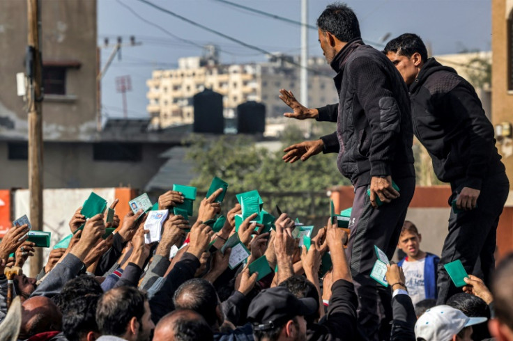 Palestinians wave their identity cards as they gather to receive flour rations for their families outside a warehouse of the UN Relief and Works Agency for Palestine Refugees in Rafah in the southern Gaza Strip