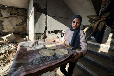 A mother and her daughter prepare traditional bread in their destroyed house in Rafah in the southern Gaza Strip on December 18, 2023
