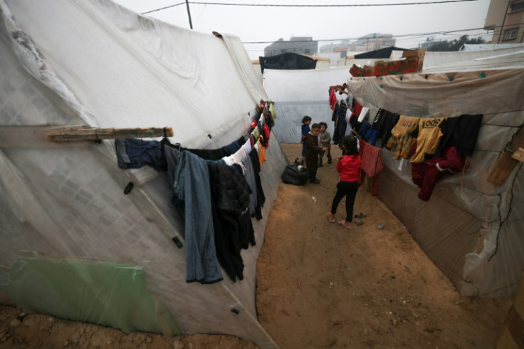 Laundry hangs on makeshift shelters as children play at a camp for displaced Palestinians in Rafah on the southern Gaza strip on December 28, 2023
