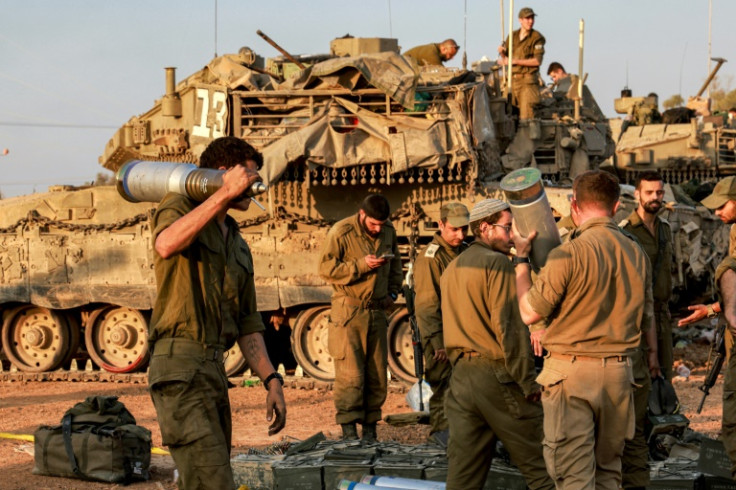 An Israeli soldier carries a shell past battle tanks deployed at a position along the border with the Gaza Strip and southern Israel on December 31, 2023