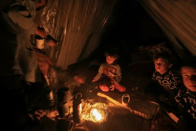 Displaced Palestinian children sit by the fire at a makeshift camp west of Rafah