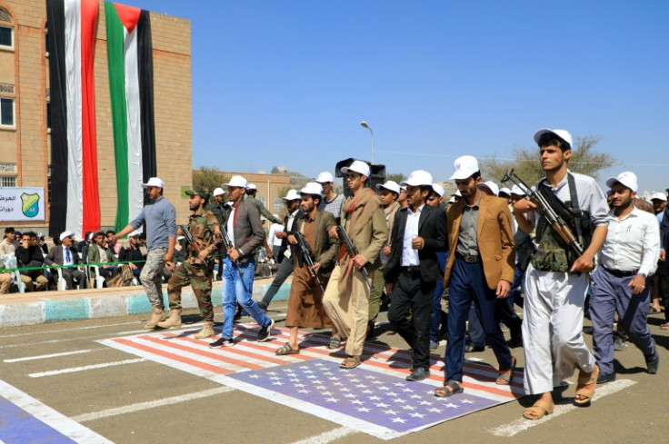 Students recruited into the ranks of Yemen's Huthi rebels hold automatic rifles as they parade over a US flag during a rally in Sanaa on February 21, 2024