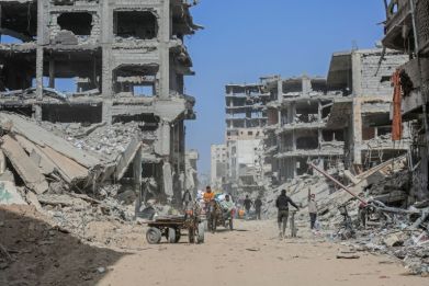 Displaced Palestinians carry belongings between bombed-out buildings in Khan Yunis