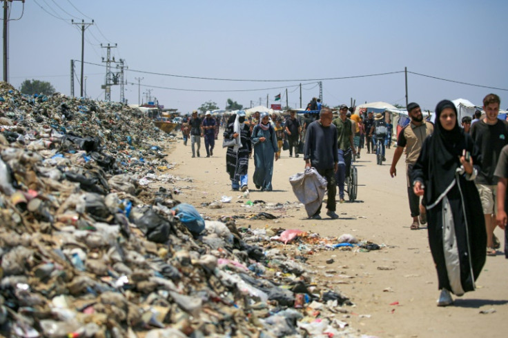 Gazans walk past piles of rubbish in Khan Yunis in the southern Gaza Strip on June 23, 2024
