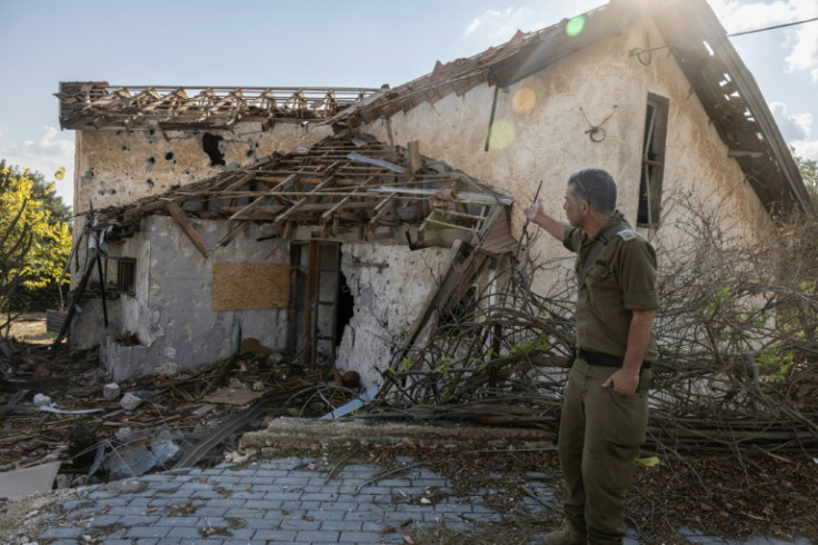 An Israeli soldier points at a house hit by Hezbollah rocket fire in the deserted northern Israeli town of Metula