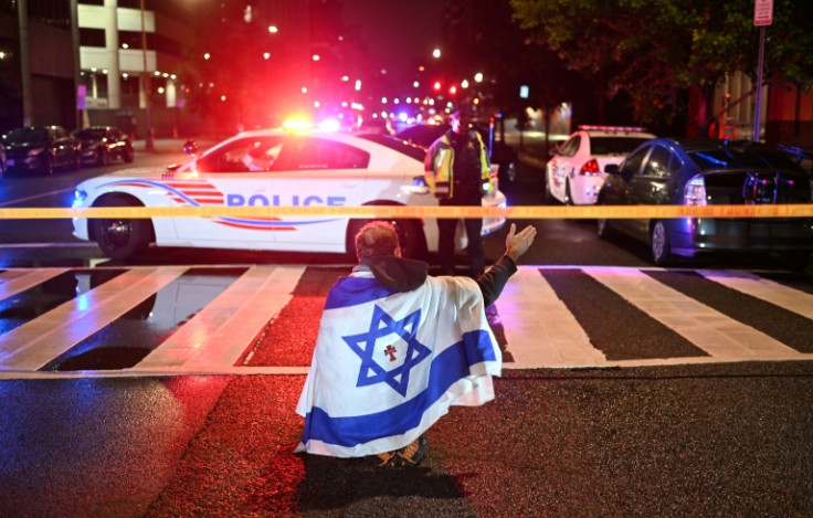 A man draped in the Israeli flag, bearing a cross and the name "Jesus" at its center, gestures as Metropolitan Police officers secure the area outside the Capital Jewish Museum