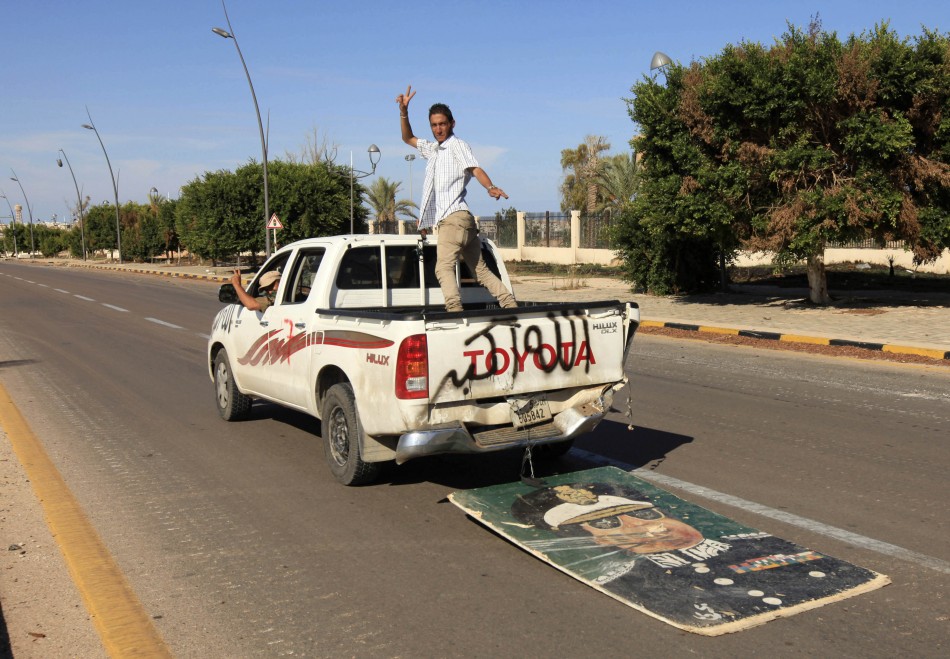 Anti-Gaddafi fighters gesture as they ride in a vehicle, trailed by an image of Muammar Gaddafi, after the fall of Sirte in the town Anti-Gaddafi fighters gesture as they ride in a vehicle, trailed by an image of Muammar Gaddafi, after the fall of Sirte in the town