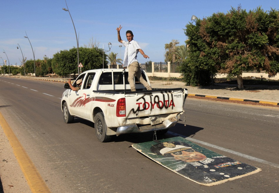 Anti-Gaddafi fighters gesture as they ride in a vehicle, trailed by an image of Muammar Gaddafi, after the fall of Sirte in the town