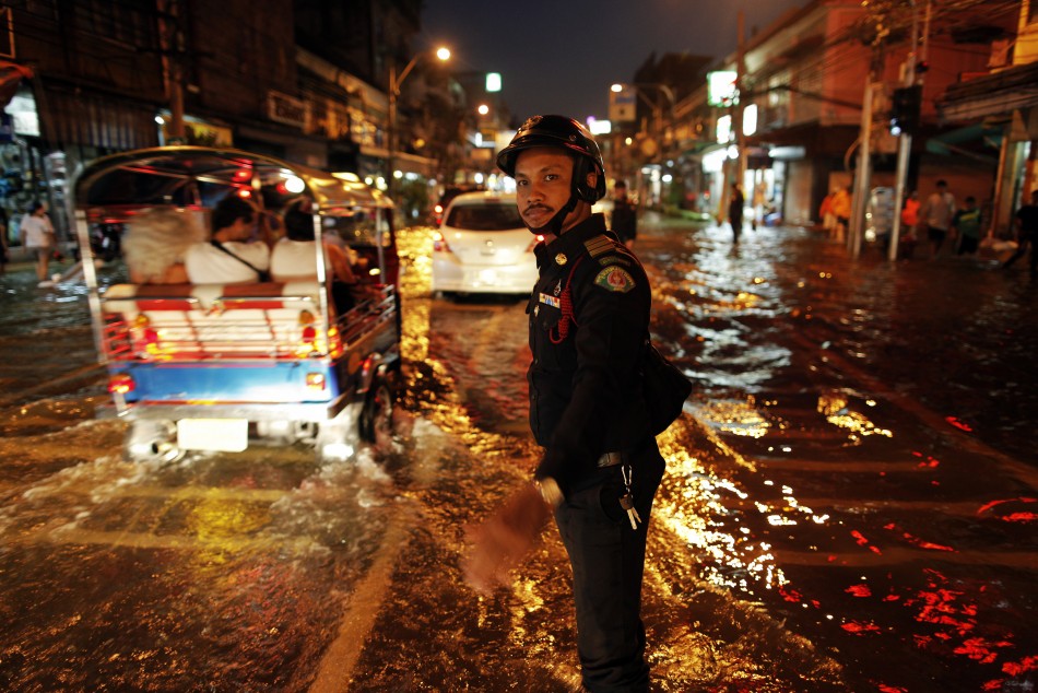 A policeman directs traffic as cars drive along a flooded street in central Bangkok