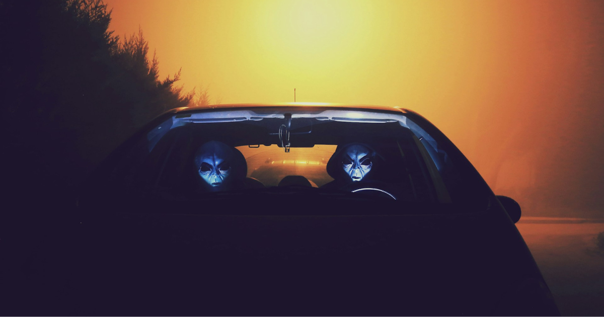 Two figures in alien mask in a car