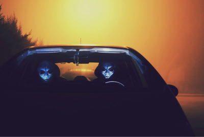 Two figures in alien mask in a car