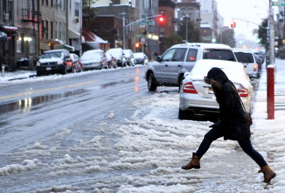 A woman tries to jump over a puddle during an early snow storm in New York