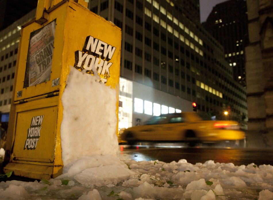 A taxi traverses down Fifth Avenue past a newsstand hit by snow in New York