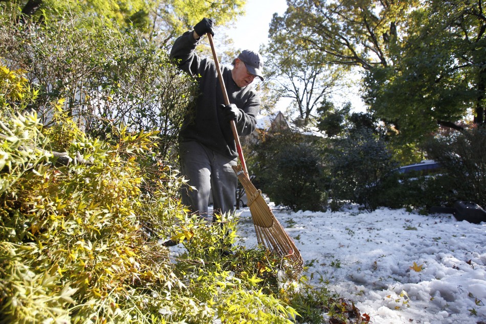 Michael Harfenist uses a rake to clear fallen branches and leaves from the snow covering his driveway in Larchmont