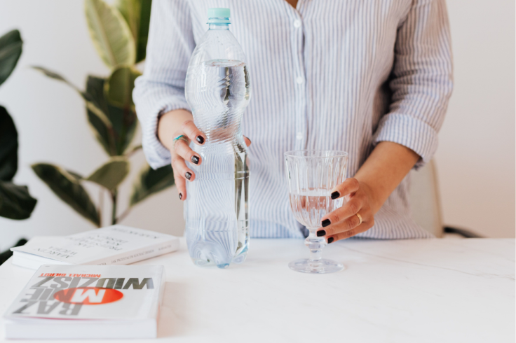A woman pours water into a glass beside books