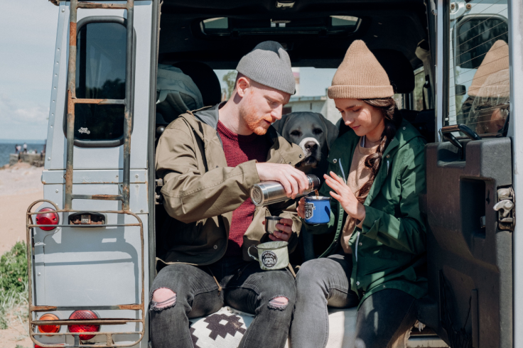 A couple pours hot drink from a thermos while sitting