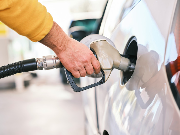 A hand holds a fuel pump nozzle inserted into a white car
