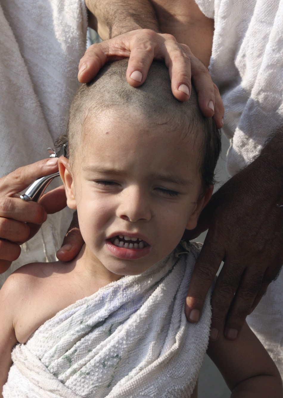A Muslim pilgrim shaves his sons head during the haj pilgrimage in Mena, outside Mecca