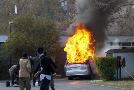 Protesters walk in the British embassy as an embassy car burns in Tehran