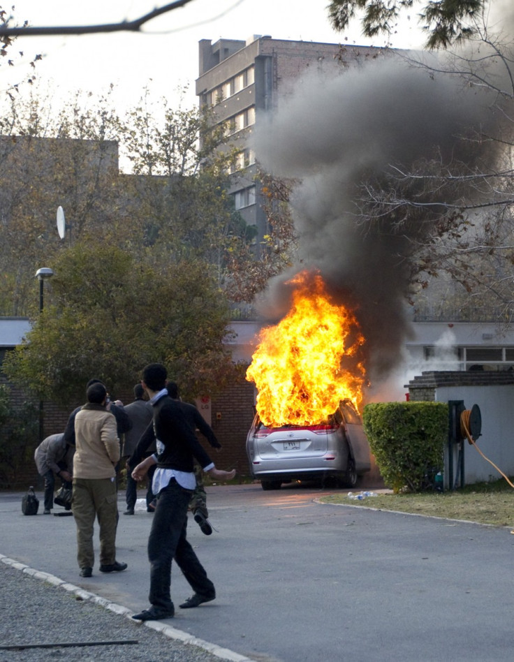 Protesters walk in the British embassy as an embassy car burns in Tehran