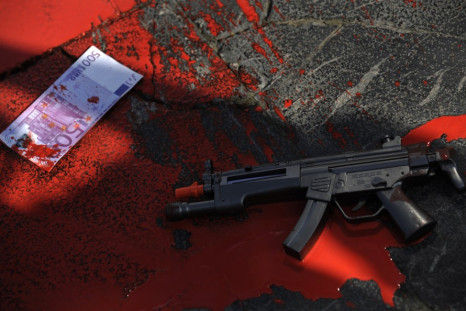 A plastic gun and a fake euro bank note lie in a pool of red paint