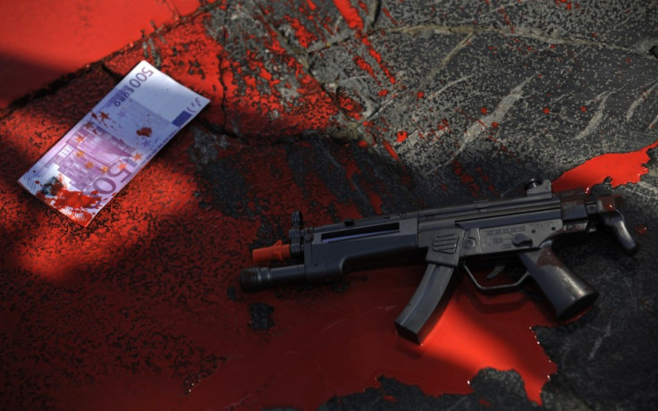 A plastic gun and a fake euro bank note lie in a pool of red paint