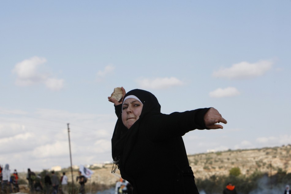 A Palestinian woman pelts a stone at Israeli troops