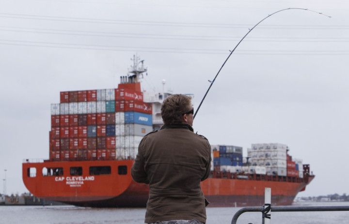A man fishes while a loaded tanker passes by A man fishes while a loaded tanker passes by