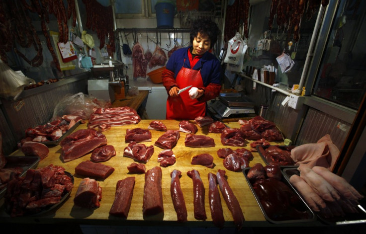 A woman cuts a pig&#039;s trotter for a customer at her small pork stall located in a meat market in central Beijing