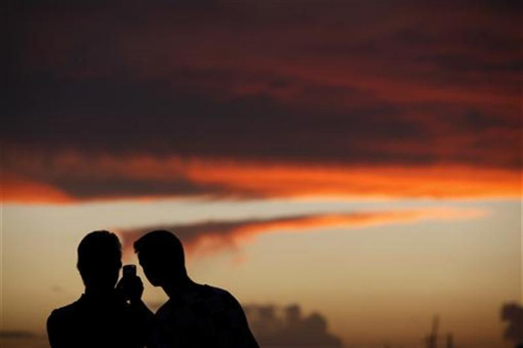 Tourists use a mobile phone to take a photo of the sunset in the town of Sliema in Valletta&#039;s Marsamxett Harbour