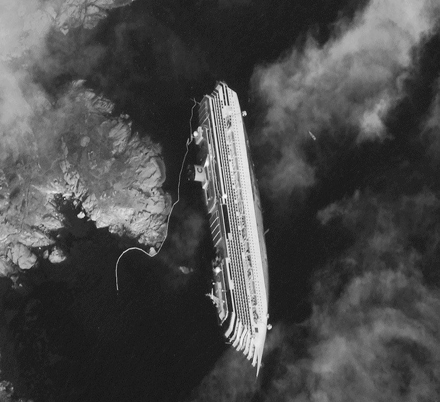 A satellite image of the Costa Concordia half-submerged in water