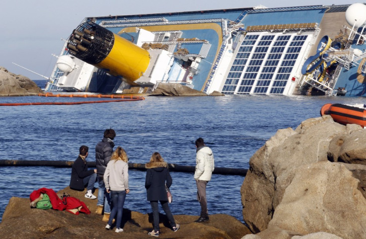 People look from a rock in front of the Costa Concordia cruise ship which ran aground off the west coast of Italy
